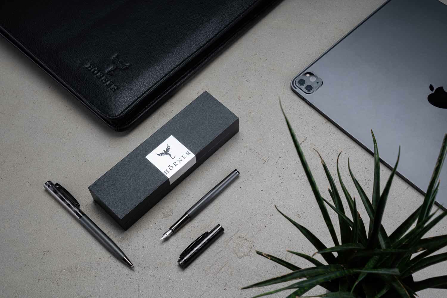 Hörner Levio Kugelschreiber und offener Füllfederhalter mit Geschenkbox, Phönix-Ledermappe und Tablet auf einem Schreibtisch