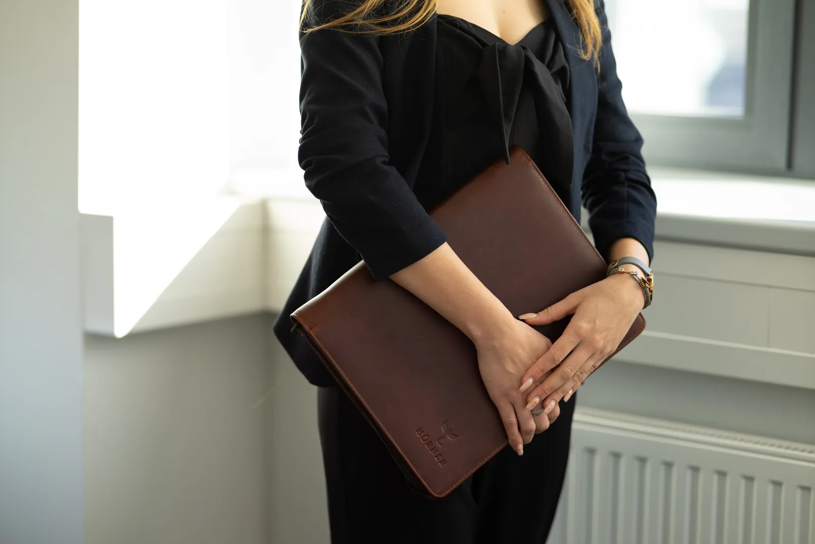 Person hält die Hörner Berlin Konferenzmappe aus Cognac-Leder an einem hellen Fenster