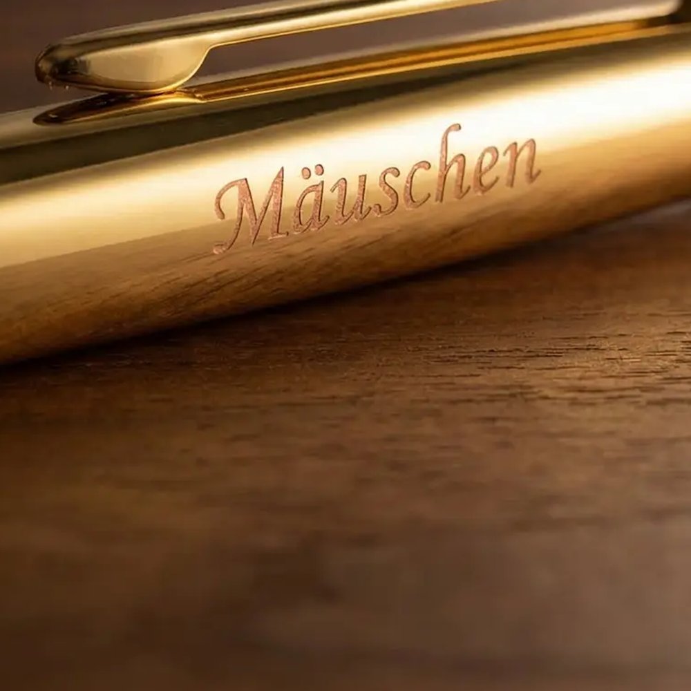 Gros plan sur la gravure manuscrite Mäuschen sur le capuchon doré d’un stylo-bille Hörner Legno