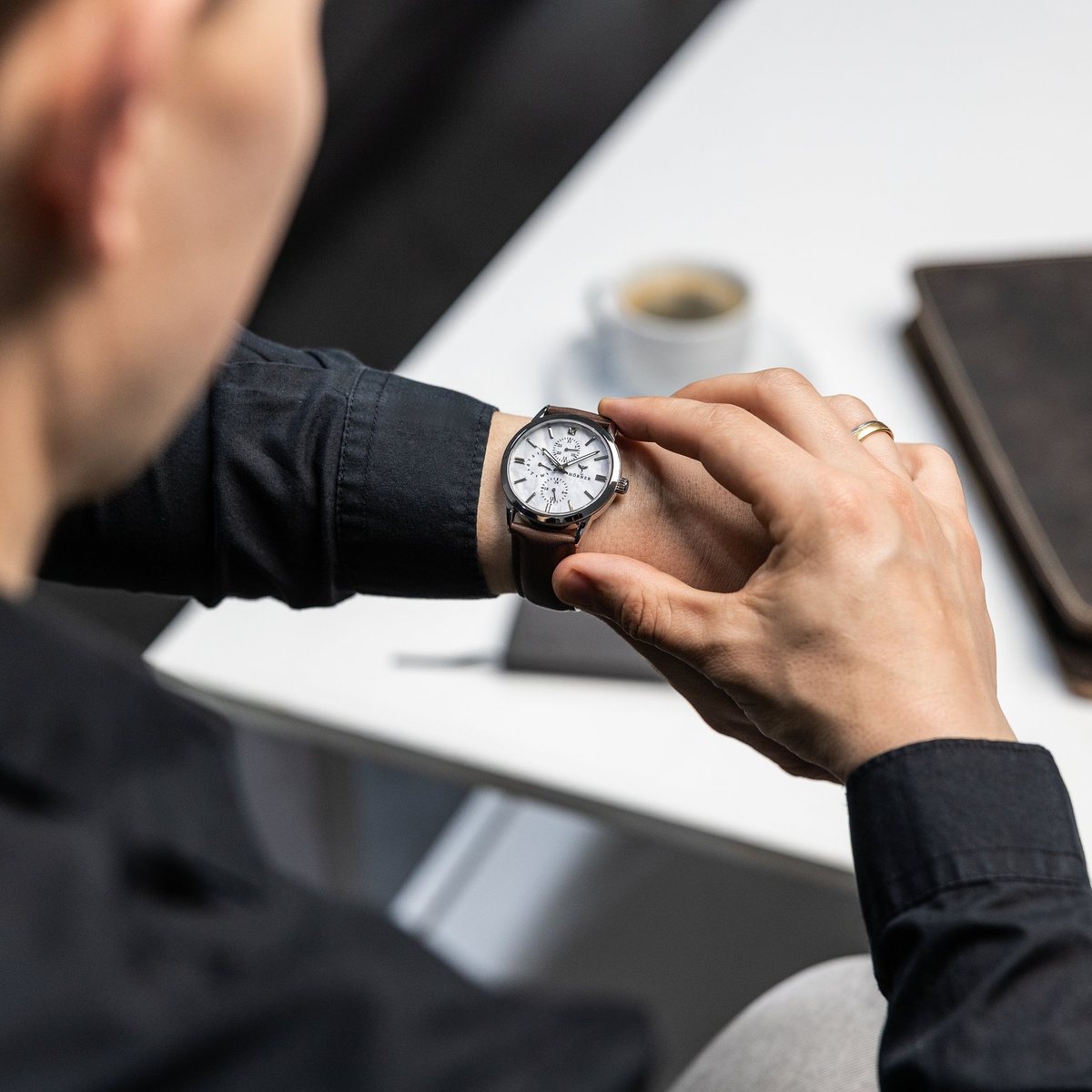 Klassische Armbanduhr mit hellem Zifferblatt und braunem Lederarmband am Handgelenk, getragen zu einem hellen Hemd