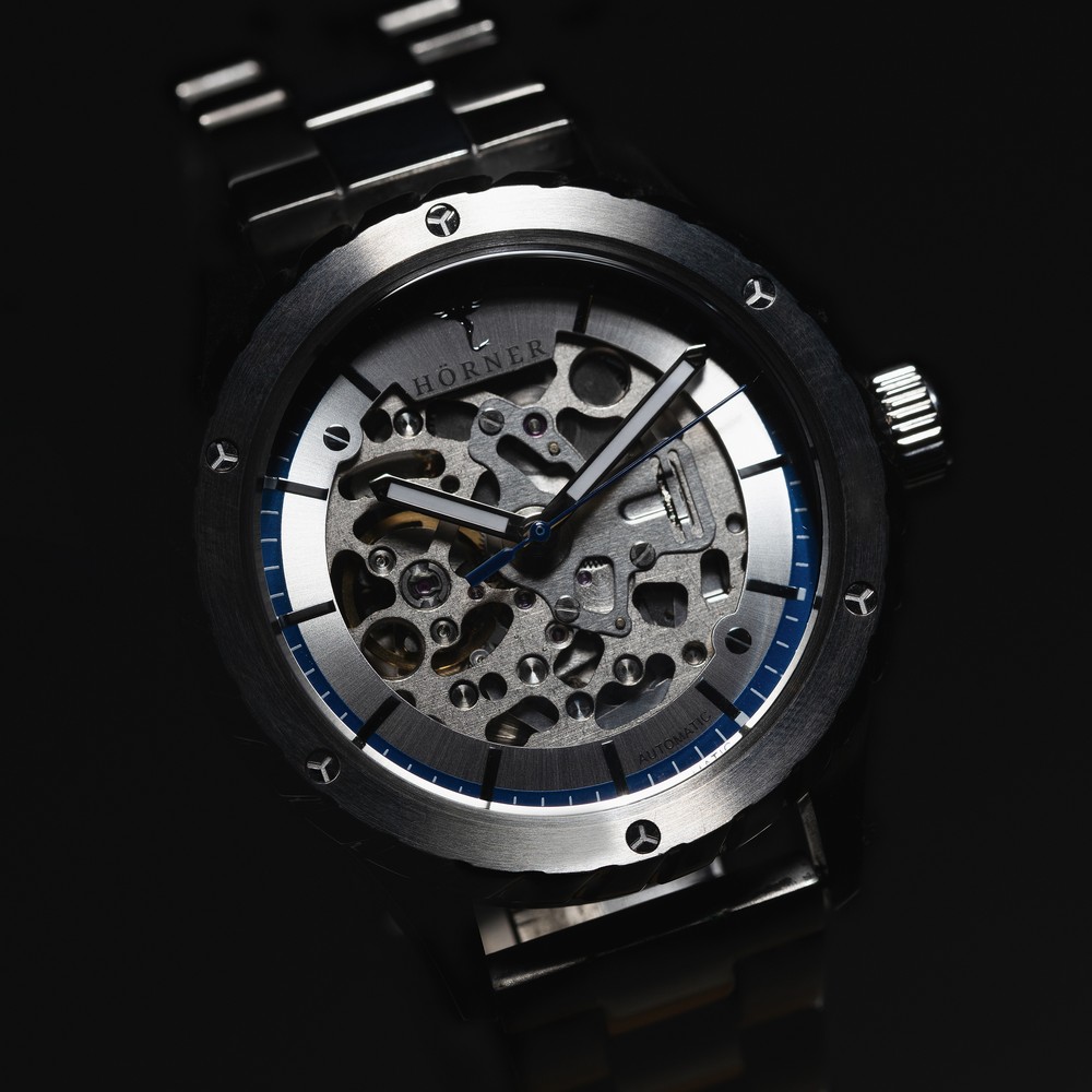 Hörner Pulsar Design mit skelettiertem Zifferblatt, blauem Minutenring, silbernem Gehäuse und Edelstahlband
