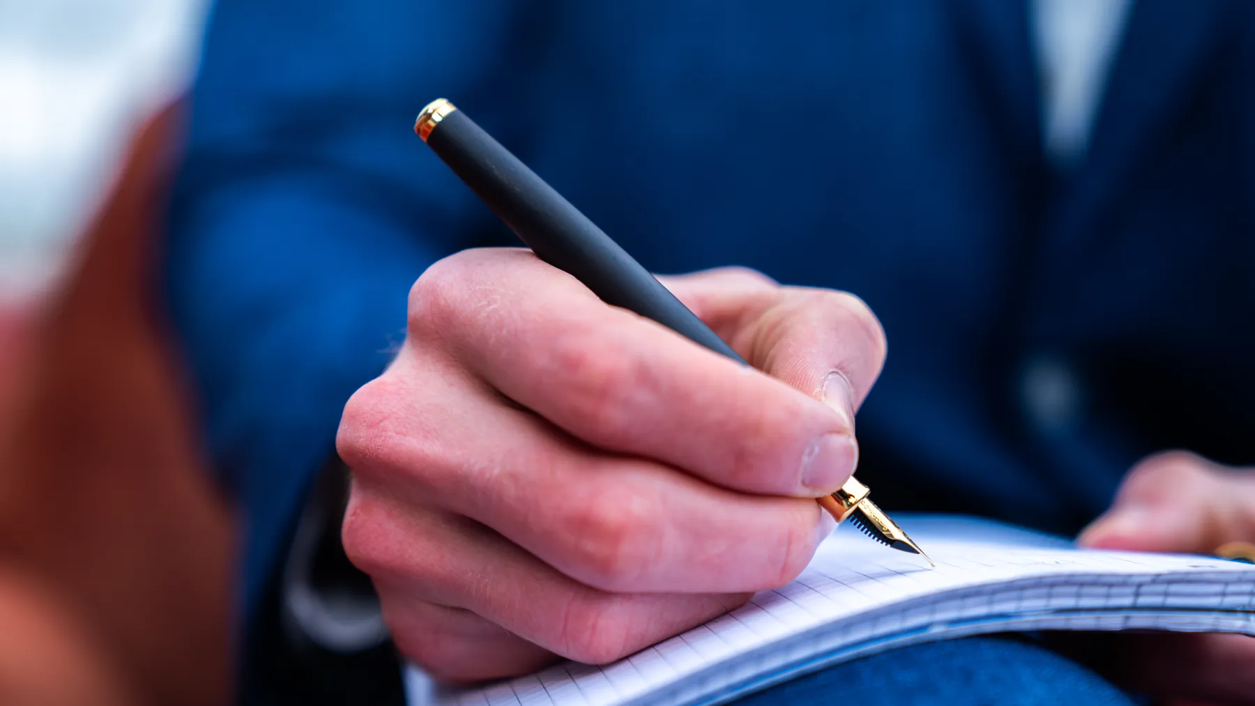 Hand schreibt mit einem schwarz-goldenen Hörner-Füllfederhalter in ein kariertes Notizbuch