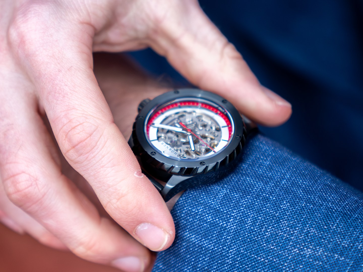 Montre automatique sportive à cadran squeletté et anneau rouge, mouvement visible tenu en main